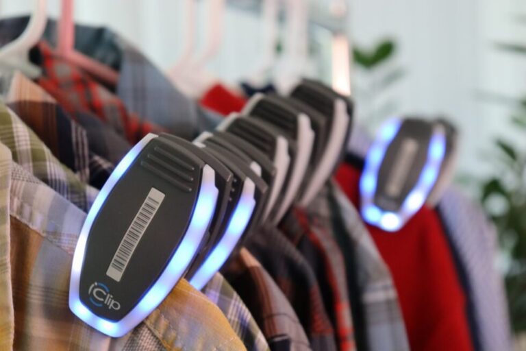 Position Imaging iClip smart tags with barcodes and glowing blue LED rings clipped to garments on a rack