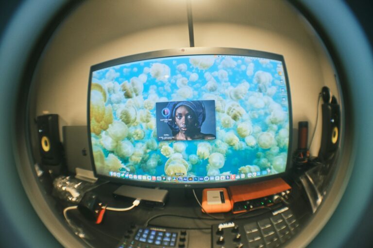 Fisheye view of a desktop workstation with a large monitor, studio speakers, and audio gear